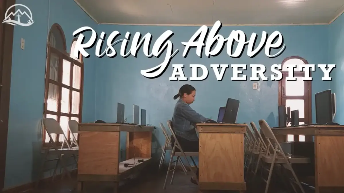 Student alone in classroom working on computer. Text: Rising above adversity