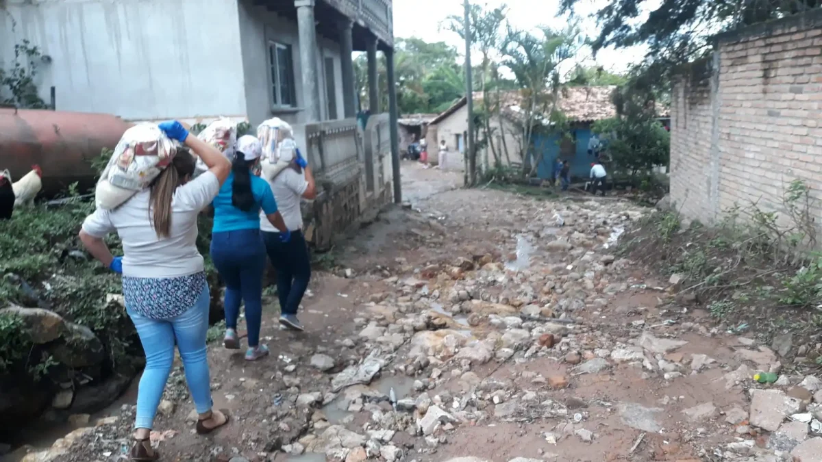 3 people walking down village lane carrying food bags